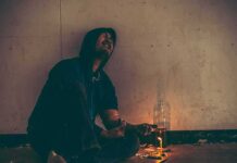 Person in hoodie sitting on floor with drug paraphernalia