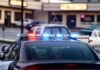 Dem Candidate ARRESTED – Handcuffed in Police Car Police car with flashing red and blue lights in a parking lot