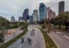 Cyclists on a curved urban road with a modern city skyline
