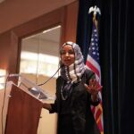 Ilhan Omar speaking at a podium with a microphone
