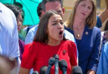 Woman in red dress speaking passionately at outdoor press conference