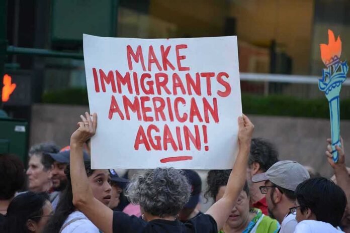Teddy Williams at a protest holding a sign reading 'Make Immigrants American Again'