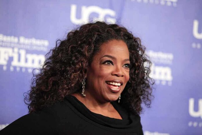 smiling woman with curly hair on a blue step-and-repeat backdrop