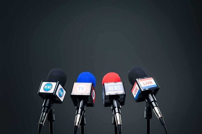 Four broadcast microphones on stands against a dark background