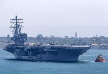Aircraft carrier escorted by a tugboat in a harbor