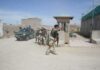 Armed soldiers patrol near a guard post outside a walled compound