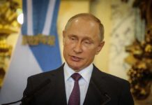 Vladimir Putin speaking at a podium with microphones
