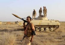 soldier carrying rocket-propelled grenade launcher in front of armored vehicle