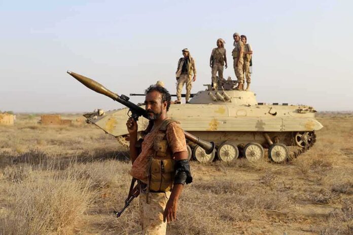 shutterstock_2391692707 soldier carrying rocket-propelled grenade launcher in front of armored vehicle