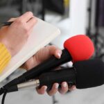 China Detains 10,000 Christians For THIS! Journalist holding two microphones while writing in a notebook