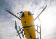 News Chopper Plunges Into Street – City Stunned! Yellow helicopter seen from below with spinning rotor against a bright sky