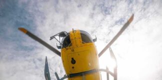 Yellow helicopter seen from below with spinning rotor against a bright sky