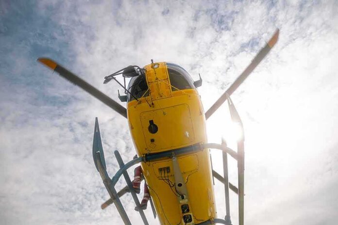 shutterstock_2461785861 Yellow helicopter seen from below with spinning rotor against a bright sky