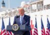 Trump Offers LAME Excuse For Rising Cost of Living Donald Trump speaking at a podium with American flags and a ship in the background