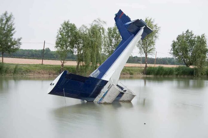 An abandoned aircraft partially submerged in a calm body of water surrounded by trees