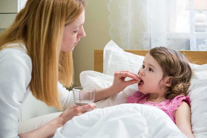 Woman giving medicine to a sick child in bed