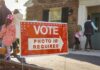 Red voting sign with arrow near people entering a polling place