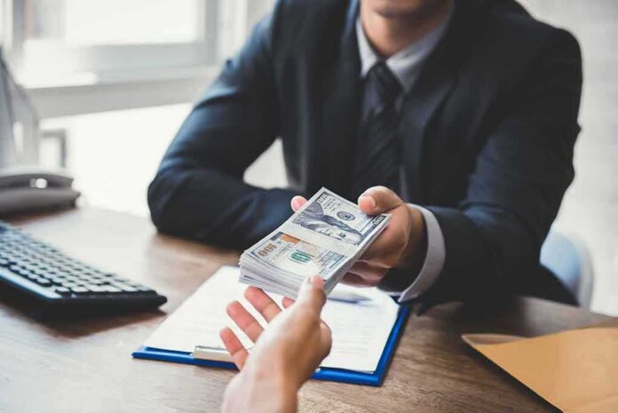 Businessperson hands over a stack of US dollars across a desk
