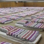 rows of mattresses with striped bedding in a large hall