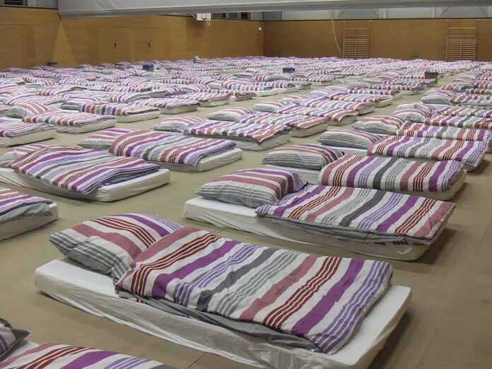 shutterstock_654873565 rows of mattresses with striped bedding in a large hall