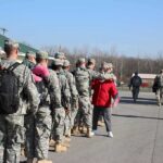 Soldiers in uniform line up outdoors with gear