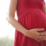 Pregnant woman in a red dress holding her belly