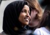 Ilhan Omar smiling in a black hijab at an outdoor event
