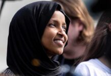 Ilhan Omar smiling in a black hijab at an outdoor event