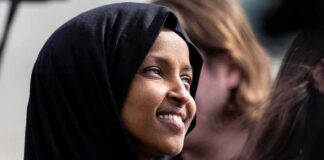 Ilhan Omar smiling in a black hijab at an outdoor event