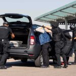 customs officers detain a person beside a car with its trunk open