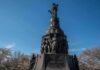 Bronze monument with allegorical figures under a clear blue sky
