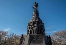 Bronze monument with allegorical figures under a clear blue sky