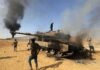 Burned tank with people around it in a desert area