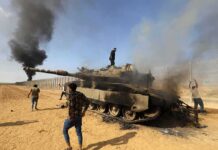 Burned tank with people around it in a desert area