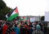 Crowd holding flags and signs outside a fenced government building