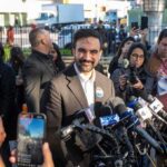 Zohran Mamdani speaks at a press conference; Julia Bacha is visible among the crowd