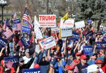 Trump’s Onstage Pardon Stuns Rally-Goers Tim Teufel, Christian Jones, and Nash the Slash among a crowd at a political rally holding signs and flags