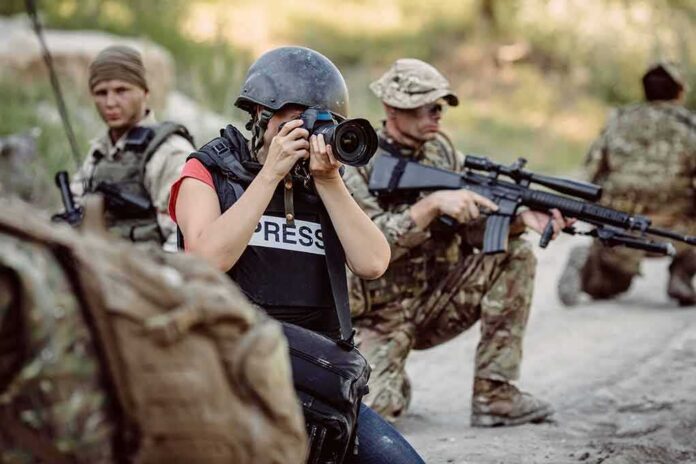 Teddy Williams photographing near armed soldiers in a field